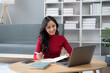 © PaeGAG - beautiful Asian girl wearing red sweater working with laptop computer in the living room.