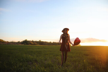 Wall Mural - A girl in a hat on a walk in the park. A girl with a basket walks in the spring. A girl is walking along the road at sunset.