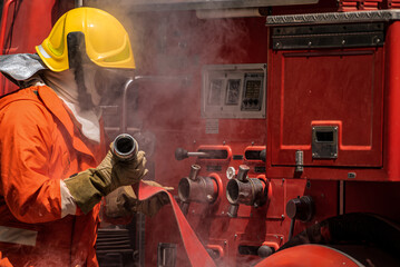 Wall Mural - With the fire hoses now ready and the firefighters poised for action they stand prepared to confront the inferno their unwavering determination evident in their focused expressions and steady hands.