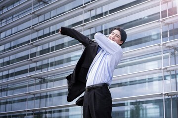 Wall Mural - Mid-career or career change image Male employee in his 30s with black hair wearing a jacket and a smile in front of an office building Copy space