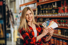 Beautiful young woman choosing paint colors and brushes at hardware store or hobby market. Young lady is shopping in the shop with do-it-yourself goods