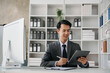 © laddawan - Young handsome man typing on tablet and laptop while sitting at the working wooden table modern office