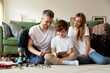 © deniskomarov - Smiling  child  with  parents siting on the floor  and watching video, cartoon  on the tablet computer