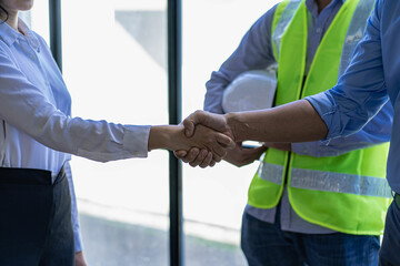 Wall Mural - Construction workers holding helmets and vests are shaking hands. real estate concept Architect shaking hands with engineer or builder planning and successful meetings