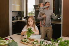Girl Holding Bok Choy With Father Carrying Son In Background At Home