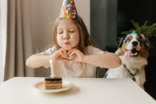 Girl Making Heart Gesture And Blowing Candle On Cake At Home