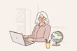 © Valery - Elderly woman teacher uses laptop sitting at table with globe and teaching students via internet