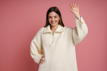 Wall Mural - Young woman smiling and waving hand while standing isolated over pink wall