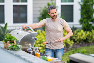 Wall Mural - Man cooking tasty food on barbecue grill outdoors. Man cooking barbecue grill at backyard. Chef preparing food on barbecue. Millennial man grilling meat on barbecue grill. Bbq party. Meal grilling.