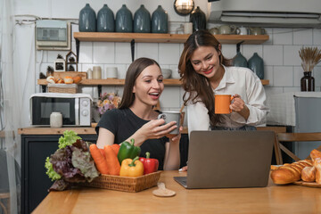 Two beautiful woman friends having breakfast and drinking coffee while talking in the kitchen at home