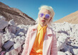 Beautiful albino girl with sunglasses, a fashion icon in a pastel suit, in a rocky desert.