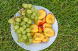 Talerz z owocami leżący na trawie. Sierpniowe zbiory w ogrodzie- nektarynki i winogrona