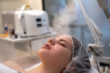 Wall Mural - Close up of beautiful woman during ozone facial steamer face treatment in beauty clinic.