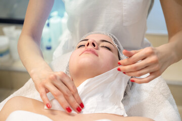 Wall Mural - Close up of young woman lying at massage table while therapist cleaning her face with paper tissue after skin treatment in spa beauty salon.