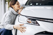 Beautiful woman hugging a car in a car showroom