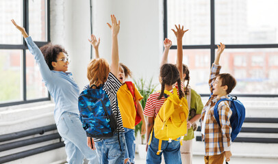 Group of schoolchildren and teacher standing together, celebrate   successful completion of collective school work and   raising their hand in class