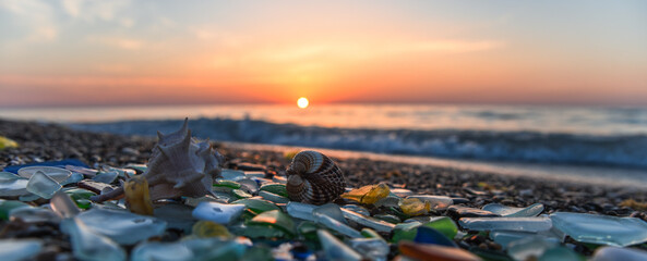 Sea glass, Natural polish textured sea glass and stones on seashore. Sunset mediterranean sea coast with waves. Green, blue shiny glass with multi-colored sea pebbles close-up. Beach summer background