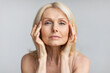 Antiage skincare. Senior woman touching skin near eyes and looking at camera, lady with flawless skin, grey background
