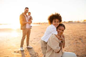 Wall Mural - Beachside bonds. Mother and son embracing and smiling at camera, father with little son standing on background