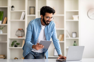 Indian Male Freelancer Working With Laptop And Digital Tablet At Home Office
