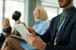 © pressmaster - Focus on tablet held by young elegant businessman in formalwear sitting against coworkers and entering data during lecture or presentation