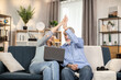 © sofiko14 - Happy couple of senior people giving high five while looking at laptop screen in cozy room interior. Elderly husband and wife in casual clothes celebrating lottery win during weekend at home.