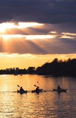 Poster - Group of people canoeing at sunset with sunrays shining through clouds