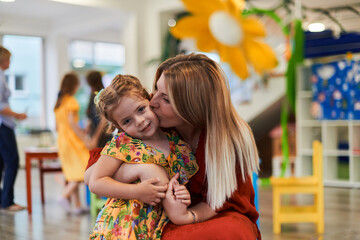 Wall Mural - A cute little girl kissing and hugs her mother in preschool