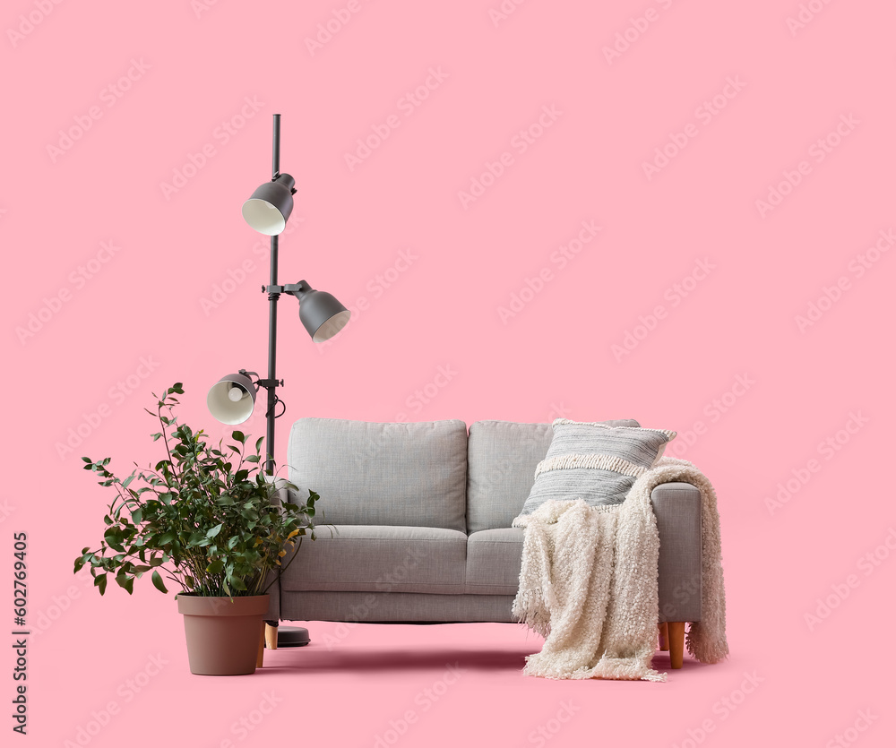 Cozy grey sofa with cushion and houseplant on pink background