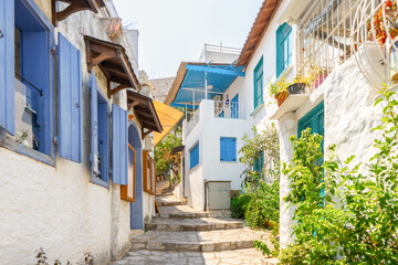 Narrow street in old european town in summer sunny day. Beautiful scenic old ancient white houses, cafe and shops with green plants. Popular tourist vacation destination, mediterranean architecture