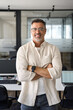 © Stock 4 You - Vertical portrait of handsome hispanic senior business man with crossed arms smiling at camera. Indian or latin confident mature good looking middle age leader male businessman on blur office back.