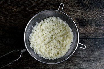 Wall Mural - Thawed Frozen Cauliflower Rice in a Mesh Strainer: Rice cauliflower in a colander placed over a mixing bowl