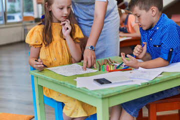 Creative kids during an art class in a daycare center or elementary school classroom drawing with female teacher.