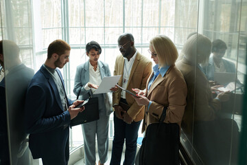 Poster - Group of intercultural employees looking through points of their reports while moving in elevator and preparing for forthcoming conference