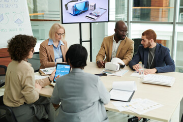 Poster - Several intercultural coworkers in formalwear discussing working points and networking while sitting by table in boardroom or office