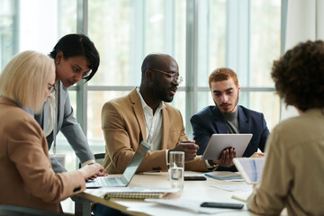 Poster - Confident analyst with tablet explaining online data to colleague during discussion of financial graphs and charts among coworkers in office