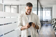 © Stock 4 You - Smiling mature Latin or Indian businessman holding smartphone in office. Middle aged manager using cell phone mobile app. Digital technology application and solutions for business success development.