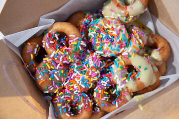 Wall Mural - A top down view of a box of mini donuts, featuring rainbow sprinkles and icing.