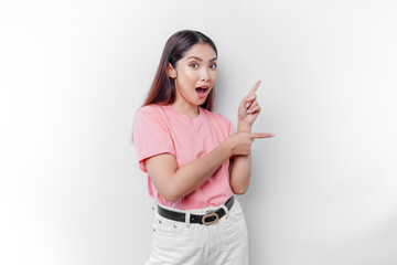 Wall Mural - Shocked Asian woman wearing pink t-shirt, pointing at the copy space on beside her, isolated by white background