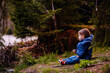 © Oleksii Yemelianov - Little toddler boy in blue spring warm outfit sitting on stone in forest