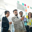 © Ruan J/peopleimages.com - Business people, teamwork and planning with sticky note, brainstorming or talk for solution, idea or goal. Group, glass board and focus with concentration for proposal, project or team in workplace