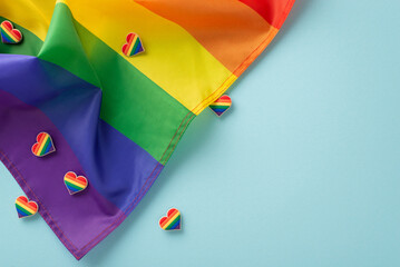 Wall Mural - LGBTQ History Month concept. Top view flat lay of rainbow-themed parade accessories, symbolic flag, and pin badges on pastel blue background with empty space for text or ad