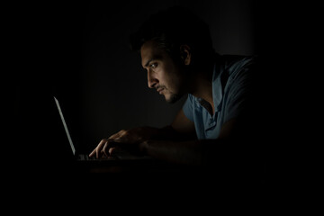 Side view of young handsome man working on laptop at night. Work from home concept	