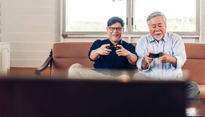 Wall Mural - Portrait of happy love asian family senior mature father and young man adult son having fun enjoy holding gamepad controller play console video game together at home