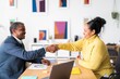 © Studio Marmellata - Side view of smiling Ethiopian woman and man in smart casual clothes shaking hands after successful discussion while looking at each other in modern office