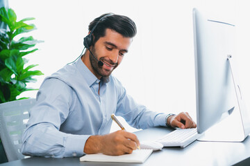 Male call center operator or telesales representative siting at his office desk wearing headset and engaged in conversation with client providing customer service support or making a sale. fervent