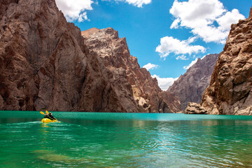 Wall Mural - Kayaking on a mountain lake. Two men are sailing on a red canoe along the lake along the rocks. The theme of water sports and summer holidays.