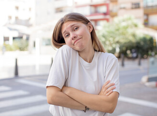 Wall Mural - pretty young woman shrugging, feeling confused and uncertain, doubting with arms crossed and puzzled look