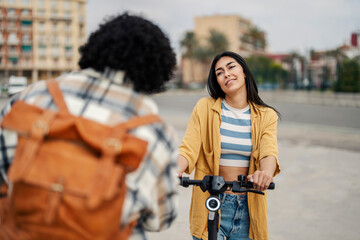 Two eco-friendly tourists are standing with an electric scooter on a street downtown and discussing sightseeing.