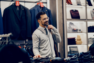 Wall Mural - A young happy smart causal man is choosing clothes at store.